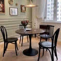 Dining room with a round wooden table and black chairs, featuring a vase of flowers and a candle.