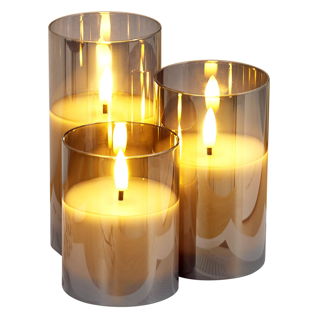 Three cylindrical glass candle holders with lit candles inside on a white background