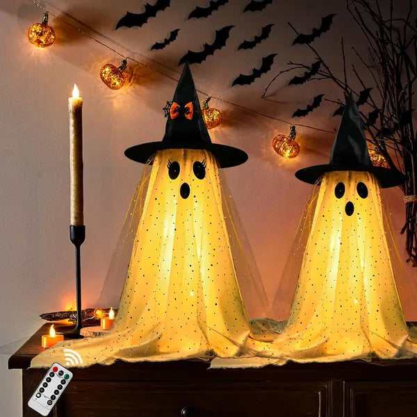 Two glowing yellow ghosts with black hats on a table, surrounded by Halloween decorations.