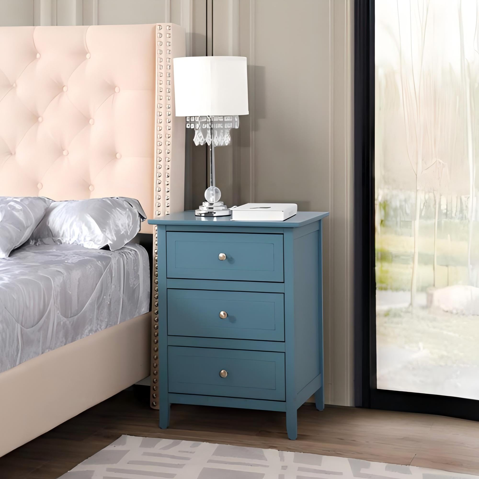 Blue nightstand with lamp and book next to a bed in a bedroom.