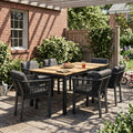 Outdoor patio set with wooden table and black chairs on a stone patio.