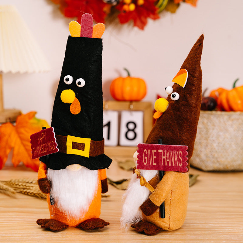 Two decorative figures resembling turkeys with hats, holding signs, on a table with pumpkins and a calendar in the background.