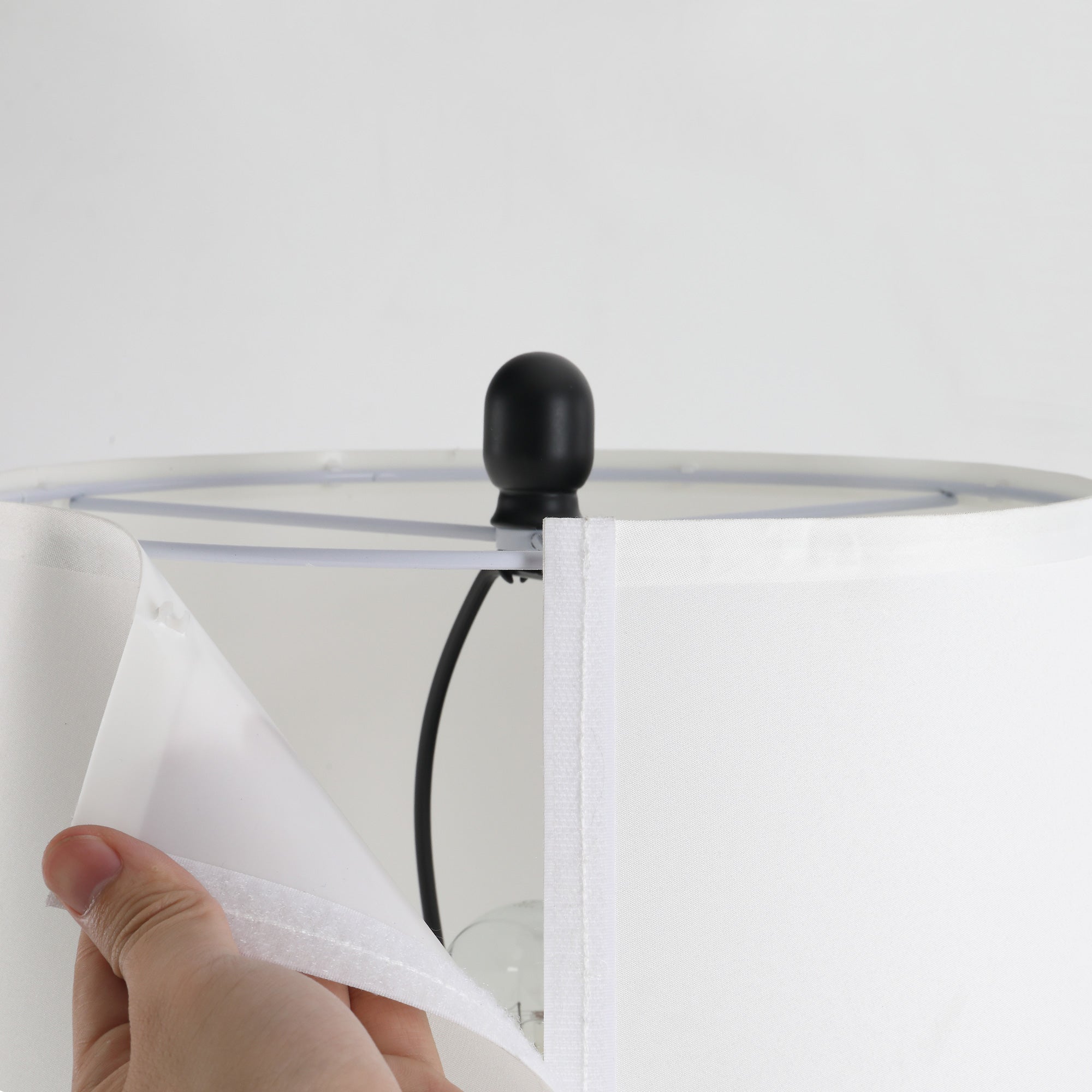 Hand holding a white fabric against a clear circular object with a black handle on a light gray background