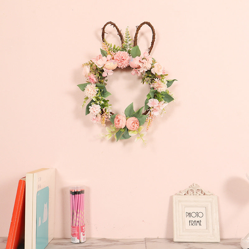 Floral wreath with rabbit ears on a pink wall, books, and a photo frame in the foreground.