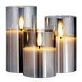 Set of three metallic candle holders with lit candles inside on a white background