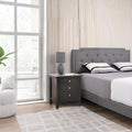 Modern bedroom with gray upholstered bed and nightstand near a window.