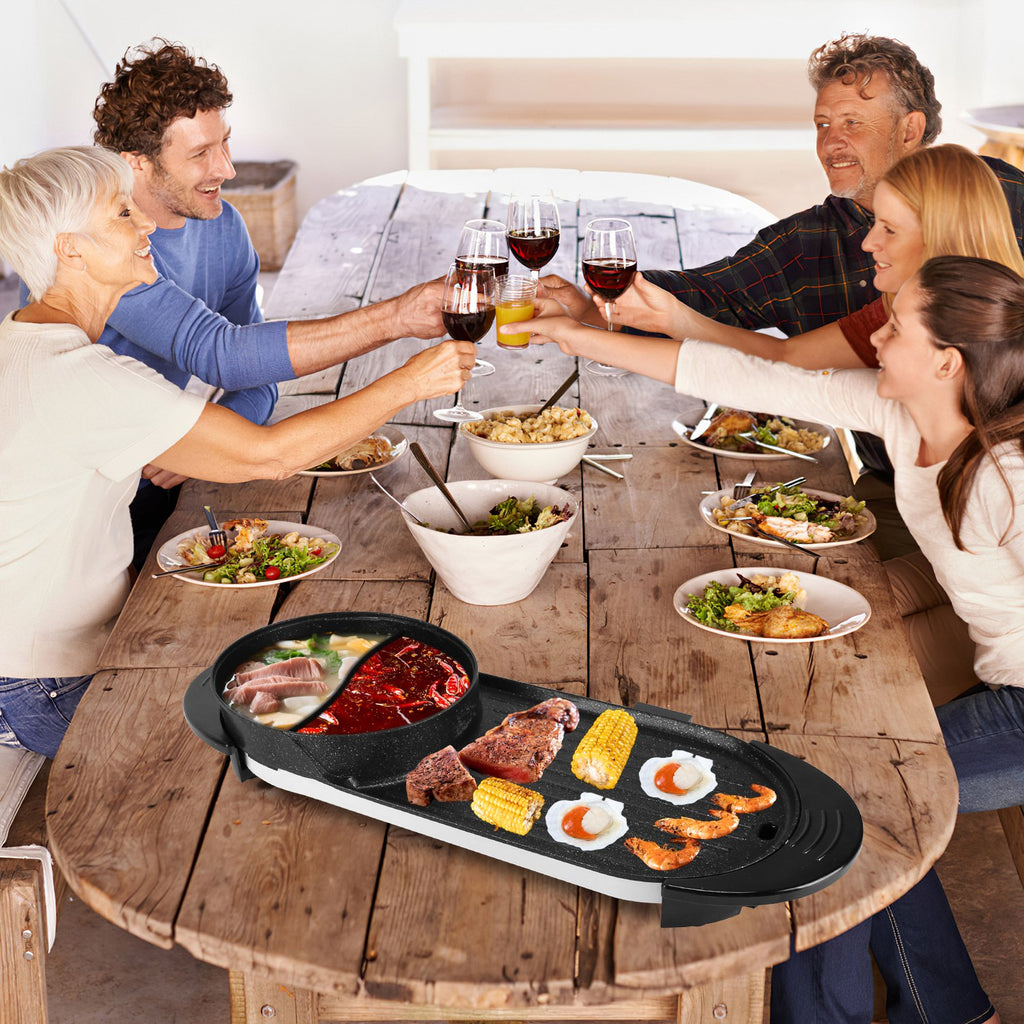 Family gathered around a wooden table with a portable grill, enjoying a meal together.