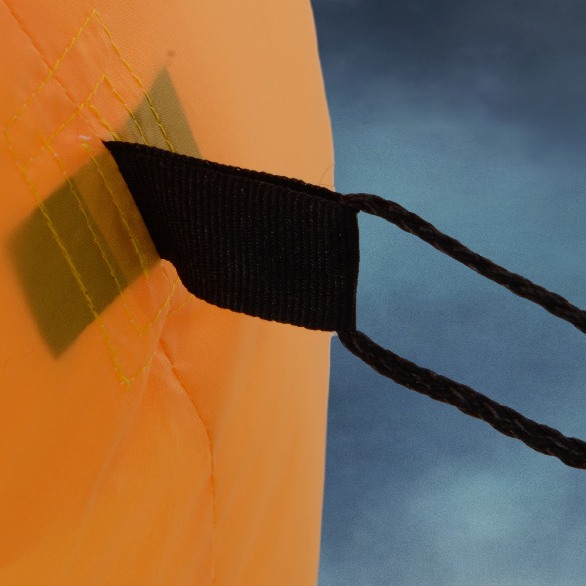 Close-up of an orange bag with a black strap against a blue sky.