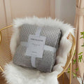 Gray textured blanket with a tag on a white furry chair