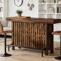 Walnut slatted wood bar table with metal footrest rail and lower storage shelf styled in a modern living room