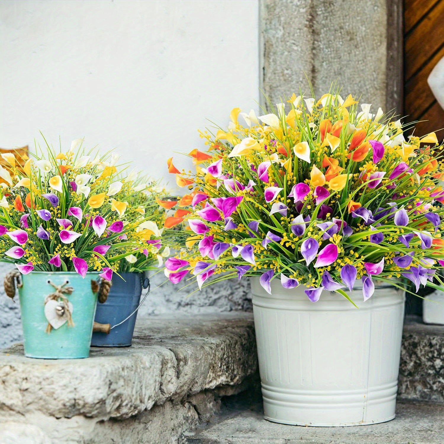 Colorful artificial flowers in metal buckets on a stone surface.