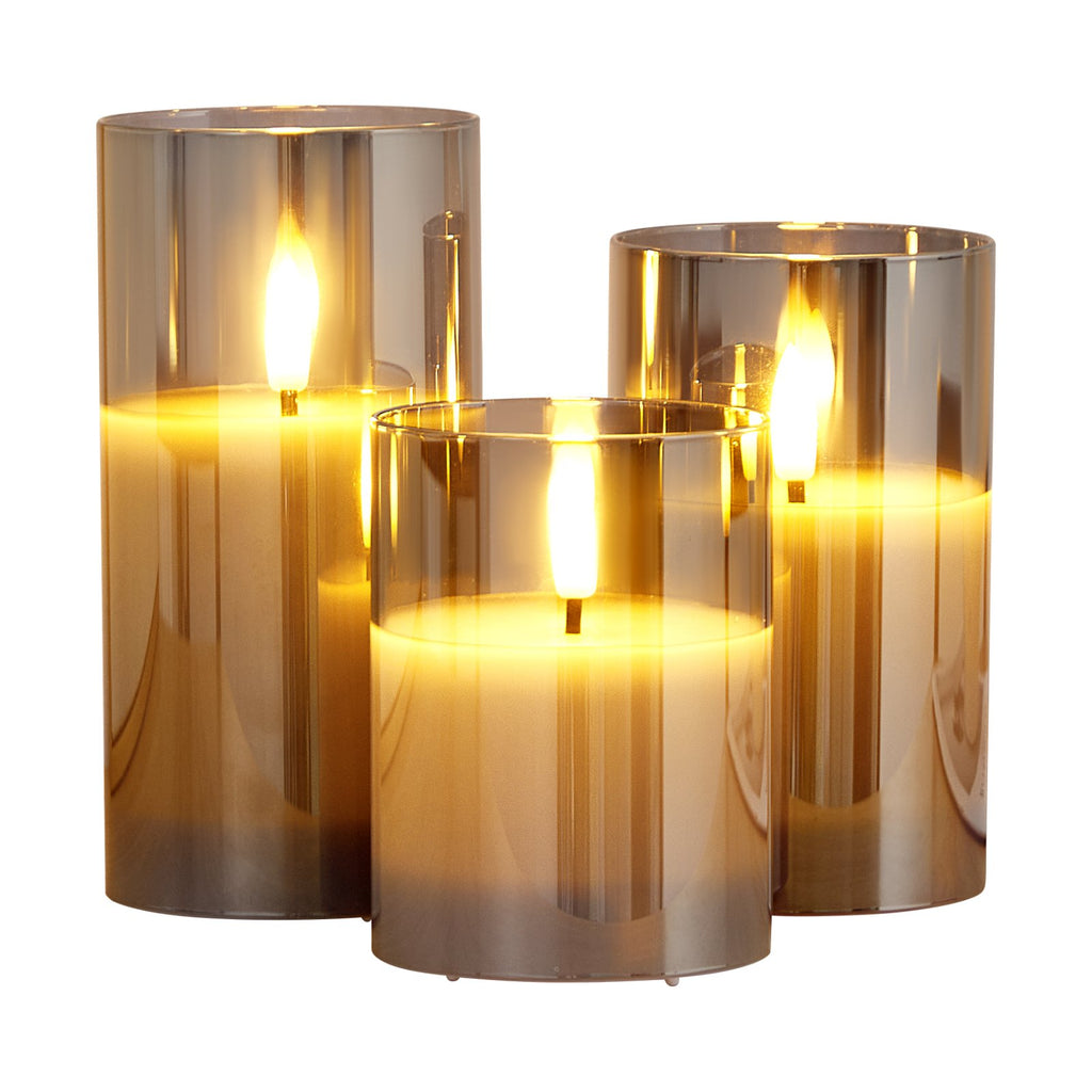 Three cylindrical candles with a warm glow in metallic holders on a white background